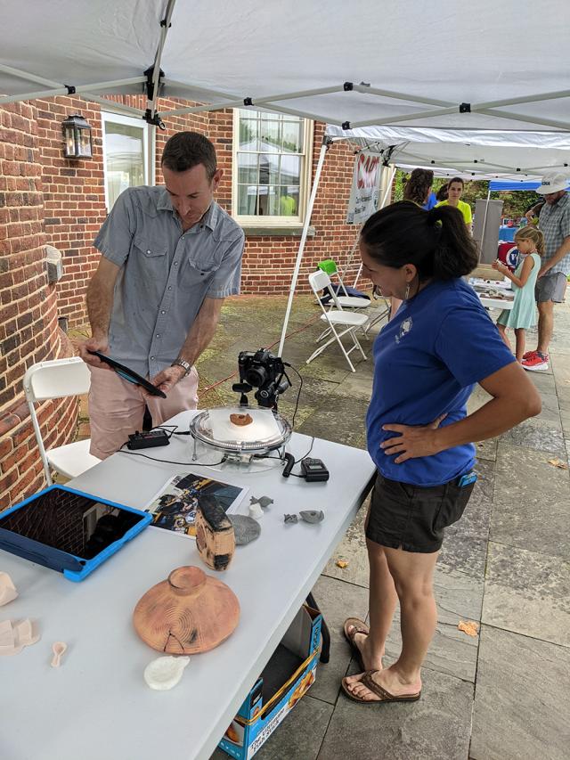 Associate Director Chris Cloke demonstrates Collaboratory's automated photogrammetry turntable to Cassandra Michaud, Archaeologist and Cultural Resources Planner for Montgomery Parks during Archaeology Day 
