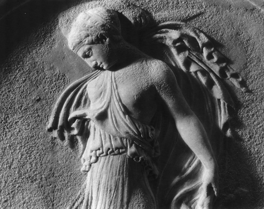Detail of ancient Greek figure of a woman with billowing drapery in low relief