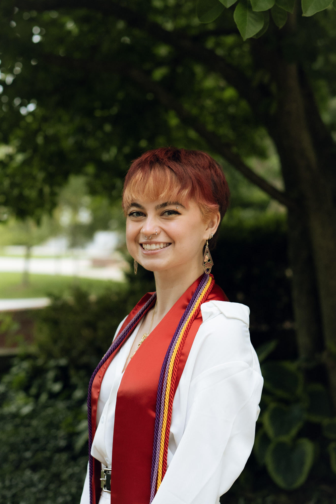 Headshot in a shade of tree of Bridget McElwee wearing graduation cords and stole.