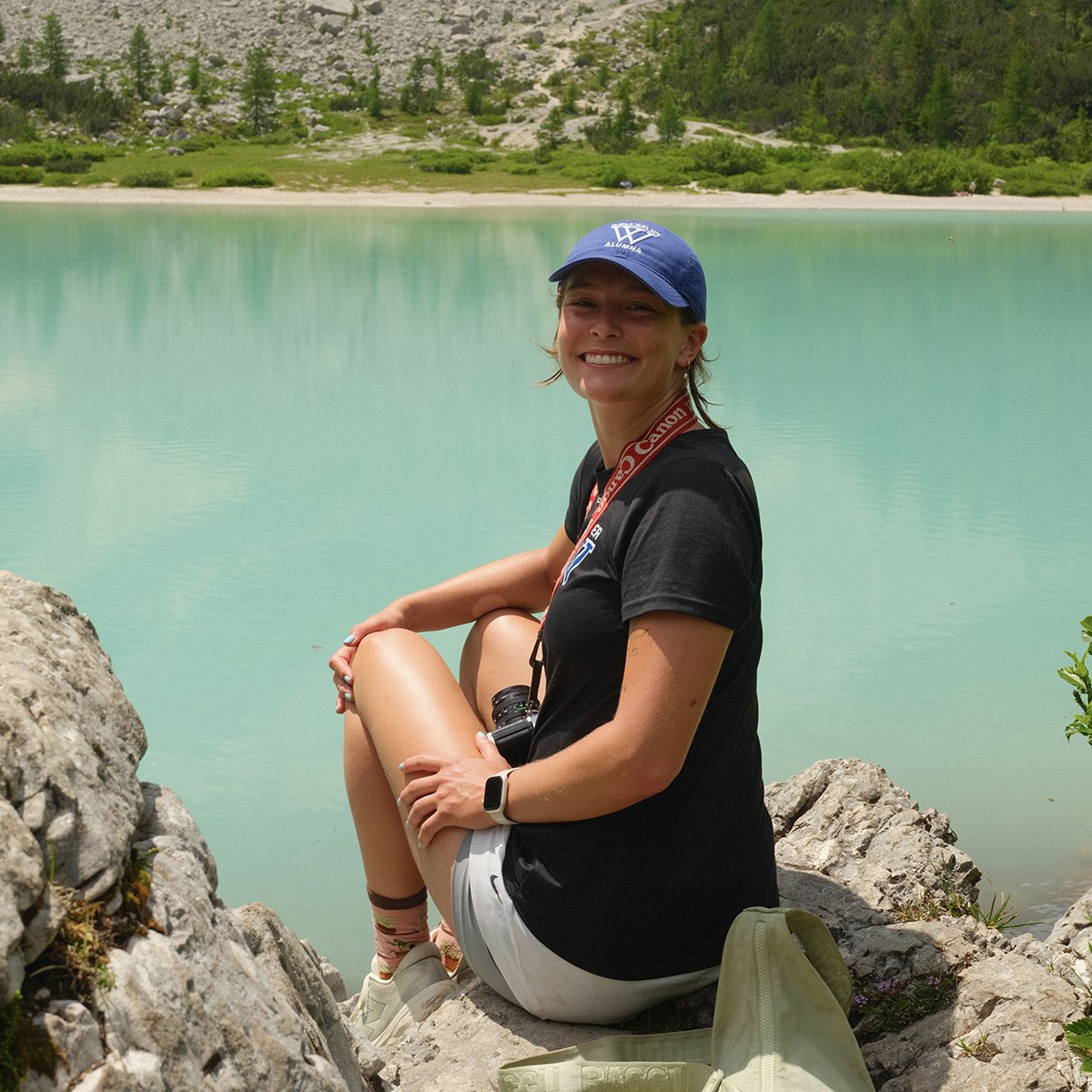 Riley McNair looking back at camera while sitting on rocky cliff overlooking glacial lake