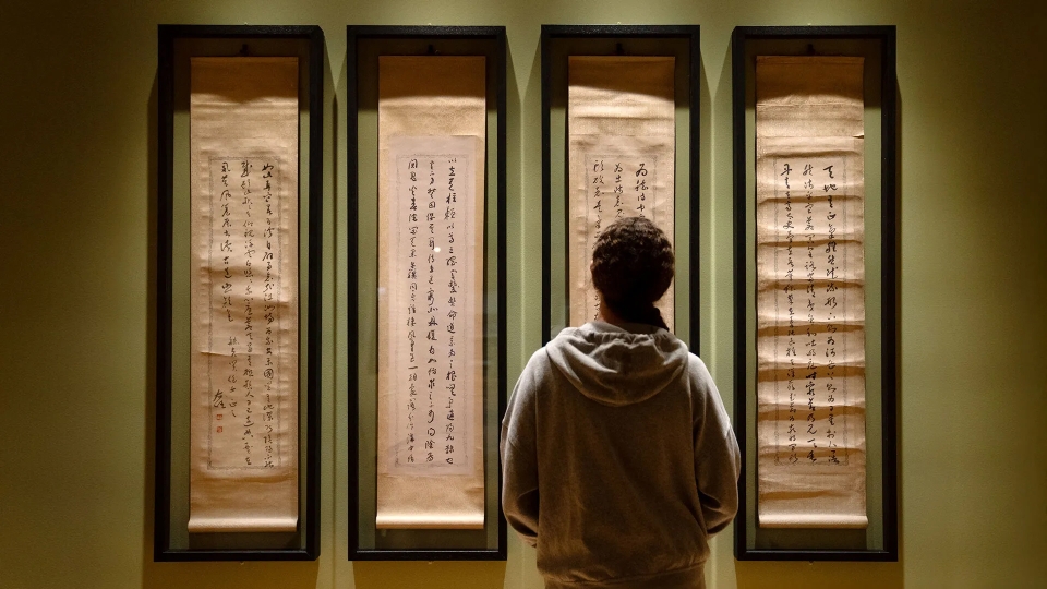 A person stands in front of four softly lit vertical Chinese scrolls in an exhibition