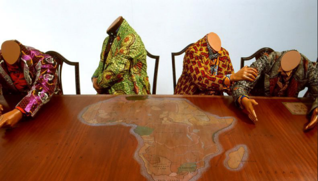 4 headless, well-attired figures (mannekins) gathered around a table with map of colonial regions of Africa inlaid